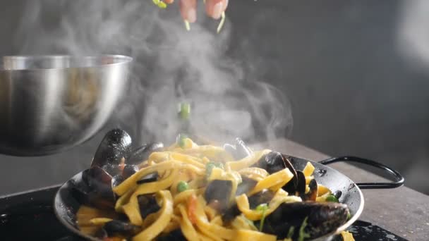 Delicious italian seafood pasta with mussels and shrimps. Chef sprinkling dish with herbs and microgreens. Slow motion. Chef hand puts herbs on top of pasta dish finished before serving. Full hd — Stock Video