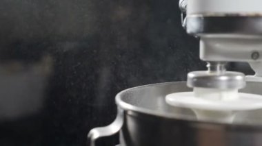 Yemek pişirme süreci. Metal kaseyle elektrikli mikser. Ağır çekim. Siyah arka planda uçuşan çiçek parçacıkları. Pasta ve fırın konsepti. Makarna, ekmek, kek, kurabiye. Tam Hd