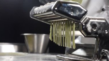 Sağlıklı İtalyan yemekleri. Makarna makinesinden makarna yapmak. Ağır çekim. Restoran yemekleri. Yuvarlanan makineden ev yapımı erişte yapıyorum. Taze spagetti geliyor. Tam Hd