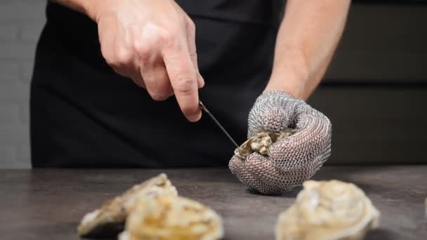 고급 해산물 식당에서. 노련 한 남성 요리사는 손에 보호용 체인메일 글러브와 특별 한 짧은 칼을 들고 신선 한 진주조개를 따 낸다. 느린 동작. 풀하드 — 비디오