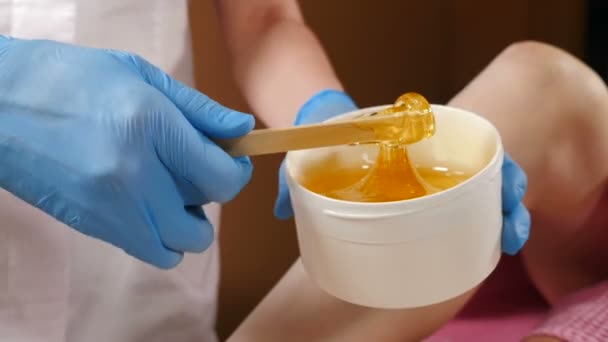 Beauty concept. Sugar paste in white jar. Beautician in blue gloves stirs sugar paste before removing hair. Sugaring. Depilation. Epilation. Paste flows down from wooden waxing spatula sticks. Full hd — Stock Video