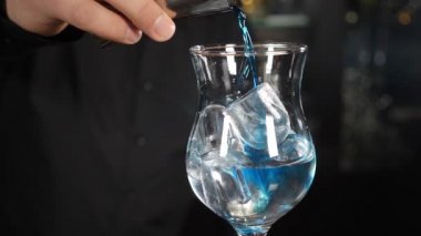 Mavi kokteyl. Barmen tezgahta ferahlatıcı renkli bir kokteyl yapıyor. Barmen siyah masanın üzerindeki buzla dolu bardağa mavi yaz kokteyli döker. Alkol kokteyli, gece hayatı ve...
