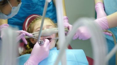 Modern diş kliniği. Gaz-oksijen anestezisi ile uzun süreli bir işlem. Küçük kız diş bakımı yaptırıyor. Bir grup diş hekimi aşırı aktif çocuk için solunum ilacı kullanıyor. 4k video