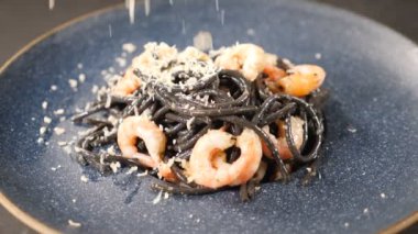 Şef taze pişmiş siyah deniz ürünleri makarnasının üzerinde sert peyniri rendeliyor. Ağır çekim. Parmesan rendelenmiş spagetti üzerine düşüyor. İtalyan mutfağı. Restoranda yemek servisi. Tam Hd