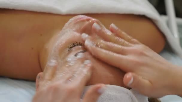 Paciente femenina disfrutando de masajes faciales relajantes en el centro de spa cosmetológico. Cuidado corporal, cuidado de la piel, tratamiento de belleza. Cara de limpieza con crema. Primer plano. Bienestar y salón de belleza. 4 k vídeo — Vídeo de stock