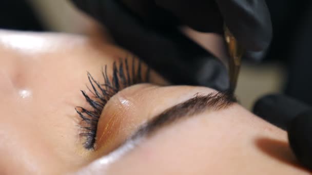 Esteticista em luvas pretas fazendo a forma permanente das sobrancelhas da correção da composição. Microblading, tatuagem de sobrancelha no salão de beleza. Mestre feminino usando agulha especial, injeta pigmento na pele. 4 k vídeo — Vídeo de Stock