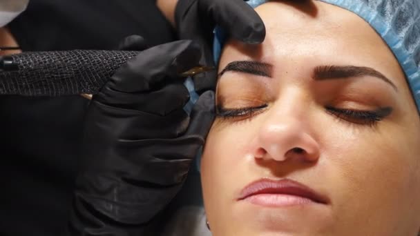 Microblading Augenbrauen-Tätowierung, permanentes Make-up. Kosmetikerin in Handschuhen spritzt mit einer speziellen Nadel Pigment in die Haut und färbt Augenbrauen. Kosmetikerin, die die Augenbrauen permanent schminkt. 4 k — Stockvideo