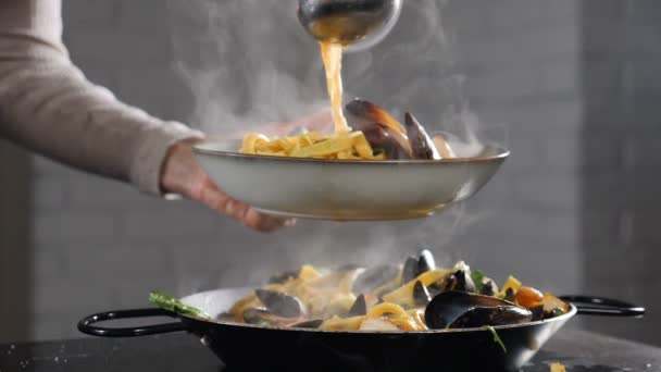 Chef serveert pasta op bord. Sluit maar af. Pasta in bord met keukentongen en pollepel. Italiaanse keuken. Witte stoom stijgt in slow motion. Damp of witte stoom stijgt op op zwart. Vol hd — Stockvideo