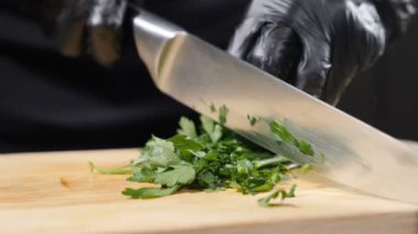 Restoran konsepti. Tahta kesme tahtasına maydanoz serpmek, ağır çekim. Siyah eldivenli şef. Mutfak bıçağıyla maydanoz doğruyorum. Maydanoz dilimleme yeşillikleri. Tam Hd