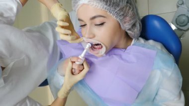 Modern diş kliniği. Ağız temizliği ve prezervatif temizliği. Hijyenik diş temizliği yapan bir kadın hasta. Doktor tedavinin bir parçası olarak dişlerini fırçalıyor. 4k video