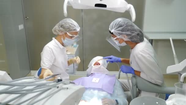 Moderne Zahnklinik. Zahnpflege. Zahnarzt und Assistentin arbeiten zusammen und tragen Kunststoff-Schutzschild, Arzt im Gesichtsschutz: Maske und Bildschirm. 4 k Video — Stockvideo