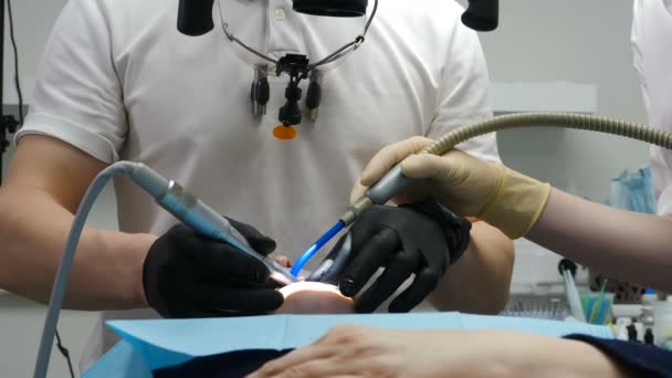 Oigenkännlig manlig tandläkare behandlar patienten. Stomatologi som gör tandkirurgi mot rotfyllningar. Tandborr, borrmaskin, professionella verktyg i läkarhänder. Begreppet tandhälsa. 4 k video — Stockvideo