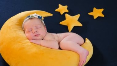 Fotoğraf çekiminde küçük bir bebek. Ay şeklinde ve yıldızlı sarı bir oyuncak üzerinde uyuyor ve poz veriyor. Sevimli, sevimli ve dokunaklı 10 günlük yeni doğmuş bebek fotoğraf bölgesinde uyuyor, çocukluk, çocukluk
