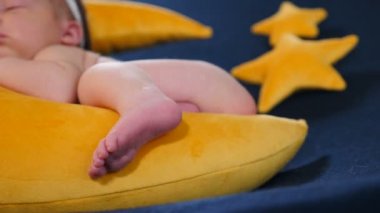 Fotoğraf çekiminde küçük bir bebek. Ay şeklinde ve yıldızlı sarı bir oyuncak üzerinde uyuyor ve poz veriyor. Sevimli, sevimli ve dokunaklı 10 günlük yeni doğmuş bebek fotoğraf bölgesinde uyuyor, çocukluk, çocukluk