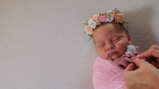 Новорожденная девочка в костюме, элегантном платье, спит в маленькой кровати, украшенной цветами. Ребенок в фотостудии. Съемки за кулисами фотографии новорожденных. 4 k видео — стоковое видео