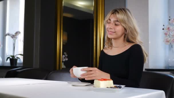 Porträtt av avslappnad ung kvinna som dricker kaffe. Vacker romantisk flicka med kopp kaffe eller te njuter fritid. ung leende kvinna lycklig i restaurang. 4 k video — Stockvideo
