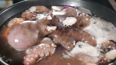 Lokanta mutfağında deniz ürünleri pişiriliyor. Lezzetli büyük ahtapot kızartma tavasında kaynıyor. Tencerede su kaynıyor. Ahtapot hazırlanıyor. Yemek videosu. 4 k video