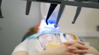 Modern diş kliniğinde profesyonel diş beyazlatma ya da beyazlatma prosedürü. LED beyazlatıcısı klinikteki sandalyede otururken koruyucu gözlüklü hasta. Ultraviyole ışınları. 4 k video