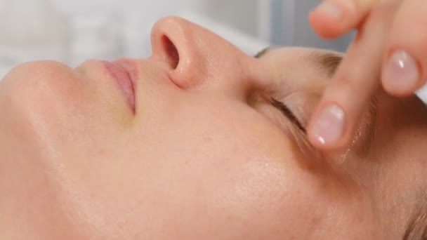 Beautist som gör botemedel på klientens ansikte på kosmetologiska kliniken. Kosmetolog läkare gör myoplastiska anti-aging ansiktsmassage sprider olja på ansiktet i skönhetskliniken. 4 k video — Stockvideo