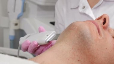 Yakışıklı genç adam kozmetik ultrasonik yüz temizliği yaptırıyor, Güzellik Uzmanı erkek yüzüne ultrason yapıyor. Erkekler için güzellik prosedürü. Donanım kozmetolojisi. 4 k video