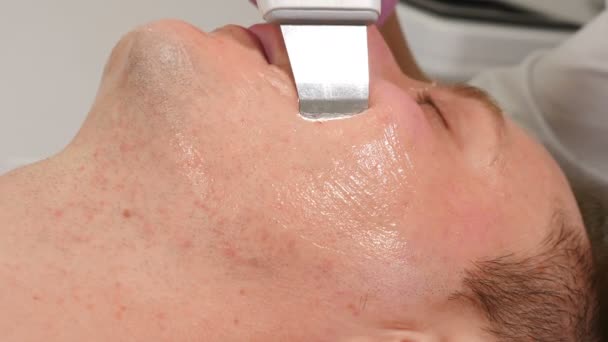 Przystojny młody człowiek, który robi kosmetologiczne ultradźwiękowe czyszczenie twarzy, kosmetyczka robiąca ultradźwięki na męskiej twarzy. Zabieg kosmetyczny dla mężczyzn. Kosmetologia sprzętu. 4 tys. wideo — Wideo stockowe
