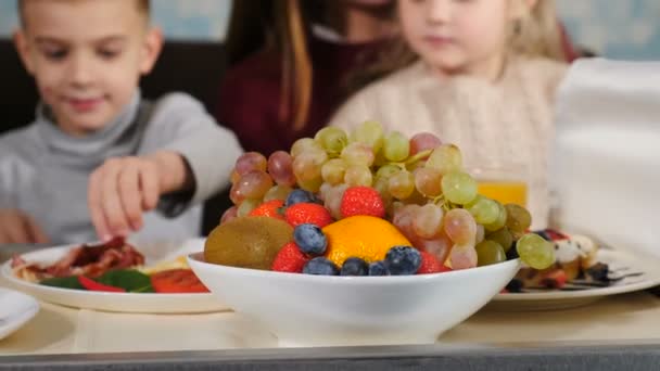 ホテルの部屋で休暇を過ごす子供連れの家族。朝食を一緒にホテルのベッドに座って。朝を楽しむ果物やジュースを食べる幸せな親。ホテルでのサービス。4 kビデオ — ストック動画