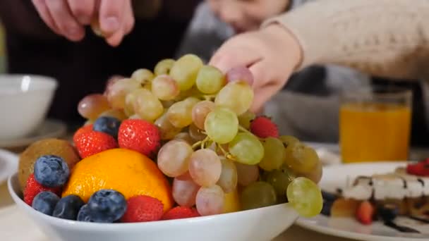 Famiglia con bambini in vacanza a riposo in camera d'albergo. fare colazione insieme seduti a letto in hotel. I genitori felici mangiano frutta e bevono succo di frutta godendo mattina. servizio in hotel. 4 k video — Video Stock