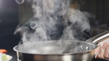 Mutfakta buhar çıkıyor. Buhar ya da Buhar bulutları ocaktaki tencerede kaynar sudan yükseliyor. Yemek pişirirken buhar çıkar. Yavaş çekimde yemek pişirmek. Buhar ve beyaz duman arka planda yükseliyor. Tam Hd