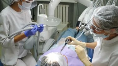 Diş hekimliği pratiği. Diş hijyeni prosedürü. Profesyonel diş büyütme. Modern dişçilikte çalışan hijyenist ve asistan. Dürbünlü mikroskop takan doktor diş temizliği yapıyor. 4 k video