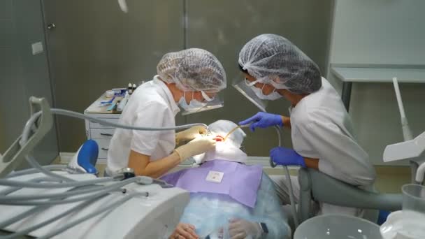 Tandläkarpraktik. Tandhygieniskt förfarande. professionell tandfjällning. hygienist och assistent på jobbet inom modern tandvård. Läkare med kikarmikroskop som rengör tänderna. 4 k video — Stockvideo