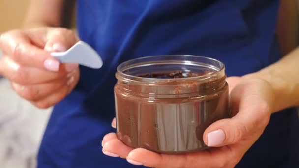 공리주의자는 초컬릿 크림 을 스파 툴라 를 탄 항아리에서 꺼내어 아름답게 처리 한다. 사이드 뷰. 화사 한 미 용법. 고급 미용 미용실에서 초콜릿으로 마사지 해 주 세요. 초콜릿 마사지 용 수술이요. 4k 비디오 — 비디오