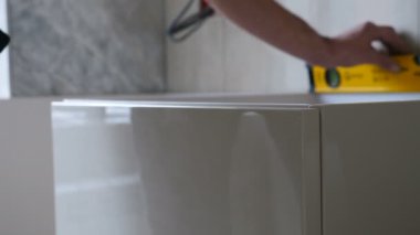 Marangoz lüks modern mobilyalar kuruyor. İşçi, su paslarını kullanarak masa yüzeyinin seviyesini kontrol ediyor. Mutfak veya banyo mobilyalarının yatay seviyelerini kontrol et. Daire tadilatı. 4 k video