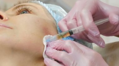 Modern güzellik kliniğinde güzellik enjeksiyonu prosedürü. Kadının yanağına şırınga enjekte edilmiş. Güzellik uzmanı güzellik salonunda mezoterapi ve yüz gerdirme tedavisi uyguluyor. 4 k video