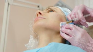 Modern güzellik kliniğinde güzellik enjeksiyonu prosedürü. Kadının yanağına şırınga enjekte edilmiş. Güzellik uzmanı güzellik salonunda mezoterapi ve yüz gerdirme tedavisi uyguluyor. 4 k video