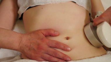 Güzellik uzmanı, genç bayan hasta için elektrikli süpürge masajı yapıyor. Güzellik kliniğinde selülit karşıtı vücut düzeltme tedavisi. Karın boşluğunda vakum masajı. Kozmetik uzmanının elleri. 4 k video
