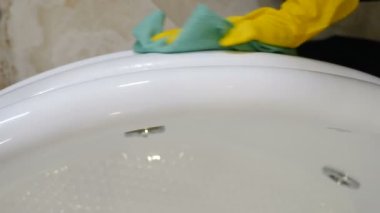 Hizmetçi ya da ev hanımı beyaz banyo yüzeyini paçavrayla siliyor. Otel dairesinde temizlik yapıyorum. Otel çalışanları lavaboyu temizleyiciyle temizliyor. Konutun banyosunda jakuzi siliyormuş.