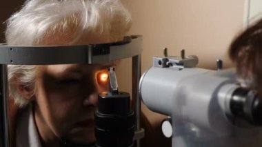 Oftalmolog, karanlık odada modern ekipmanlarla yaşlı bir kadının görüşünü kontrol ediyor. Doktor gözleri biyomikroskop cihazıyla kontrol ediyor. Tıbbi ekipmanların yardımıyla göz yapısını inceliyor.
