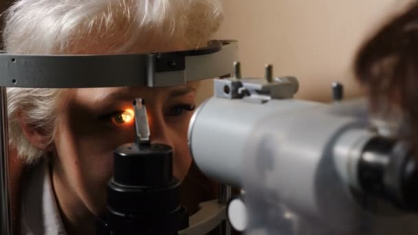 Офтальмолог перевіряє зір старшої жінки з сучасним обладнанням у темній кімнаті. Лікар перевіряє очі пристроєм біомікроскопа Доктор вивчає структуру очей за допомогою медичного обладнання — стокове відео