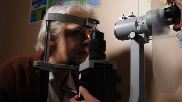 眼科医生在暗室里检查一位身穿现代装备的老年妇女的视力。医生用生物显微镜检查眼睛医生借助医疗设备检查眼睛结构 — 图库视频影像