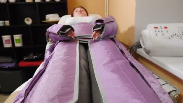 Młoda kobieta robi zabieg antycellulitowy w salonie spa. Terapeuta kosmetyczny naprawianie pasów kostiumowych i prowadzenie procedury presoterapii. Leczenie zmniejszające stężenie celulolitu. 4 tys. wideo — Wideo stockowe