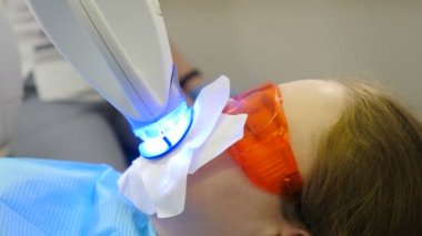 Modern diş kliniğinde profesyonel diş beyazlatma ya da beyazlatma prosedürü. LED beyazlarken koruyucu gözlüklü hasta. Ultraviyole ışınları. Diş minesi beyazlatma için lamba. 4K video