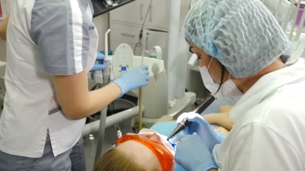 在现代牙科诊所，一组医生正在帮助女病人准备牙齿咬伤。专业的口服漂白使用紫外线灯。完美的笑与白牙齿。牙齿美白程序。4 k — 图库视频影像