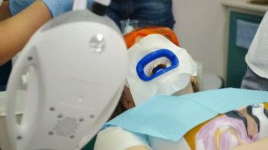 Diş beyazlatma prosedürü. Diş hekimi ultraviyole lamba kullanarak diş beyazlatıcısı yapıyor. Güzel ve mükemmel bir gülümseme. Modern dişçilik konsepti. LED beyazlarken koruyucu gözlüklü hasta. Morötesi