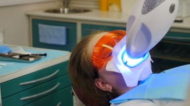 Diş beyazlatma prosedürü. Diş hekimi ultraviyole lamba kullanarak diş beyazlatıcısı yapıyor. Güzel ve mükemmel bir gülümseme. Modern dişçilik konsepti. LED beyazlarken koruyucu gözlüklü hasta. Morötesi