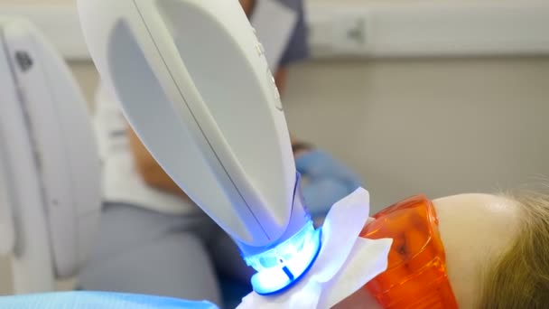 Prosedur pemutih gigi. Dokter gigi membuat pemutihan gigi menggunakan lampu ultraviolet. Senyum yang indah dan sempurna. Konsep kedokteran gigi modern. Pasien dengan kacamata pelindung sementara LED pemutih. Ultraviolet — Stok Video