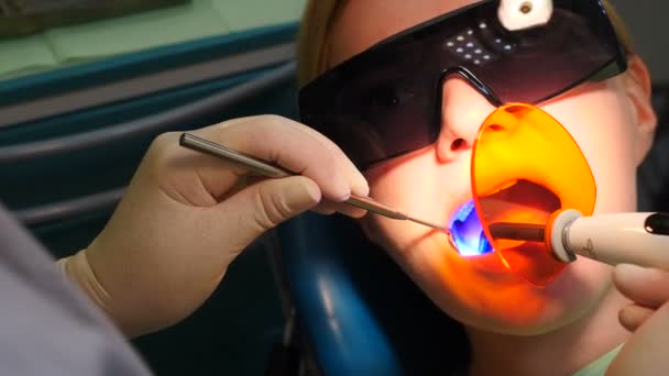 Zubař upevnění světelné výplně pomocí fotopolymer zubní bezdrátové lampy. Doktor zapne ultrafialové světlo v ústech pacientů. Moderní stomatologie. Poslední část zubní léčby. 4 k video — Stock video