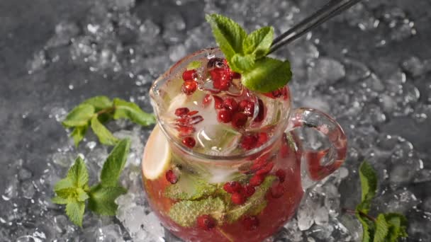 Boisson rafraîchissante d'été. Limonade pétillante de désintoxication froide avec citron vert, baies, glace et feuilles de menthe. Vue de dessus. bulles d'eau pétillante dans une cruche transparente. Des glaçons et de la glace râpée tout autour. Doucement. — Video