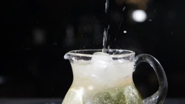 Dilimlenmiş kireç, nane yaprağı ve buzla dolu cam kavanoza soda dökülüyor. Yaz meyvesi ve böğürtlen Masada buz küpleriyle siyah arka planda taze bir kokteyl. Yavaş