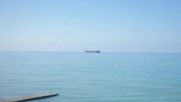 Grande nave da carico sulla linea dell'orizzonte in mare aperto, cielo azzurro e acqua blu del mare. giornata di sole luminoso, Girato dal finestrino del treno di passaggio. Maestoso paesaggio estivo. . bellissimo panorama con barca a vela in — Video Stock