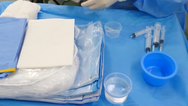 Modern klinikte damar cerrahisi hazırlığı. Cerrahi önlüklü ve eldivenli profesyonel doktorlar hastanedeki arterden trombüs çıkarmak için bir şeyler hazırlıyorlar. İnceleme için kontrast sıvısı kullanılıyor — Stok video